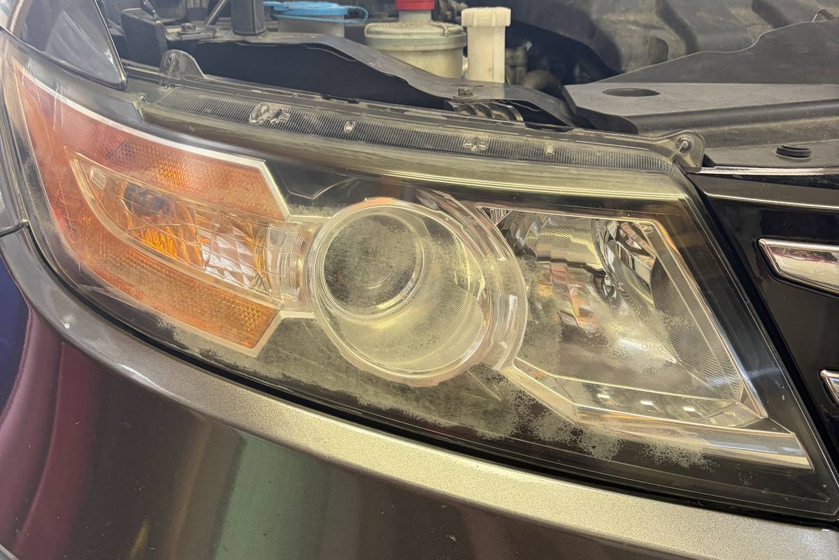 Passenger-side headlight on a grey Honda Odyssey before restoration: the lens is milky and yellowed, and the projector behind it is hard to make out