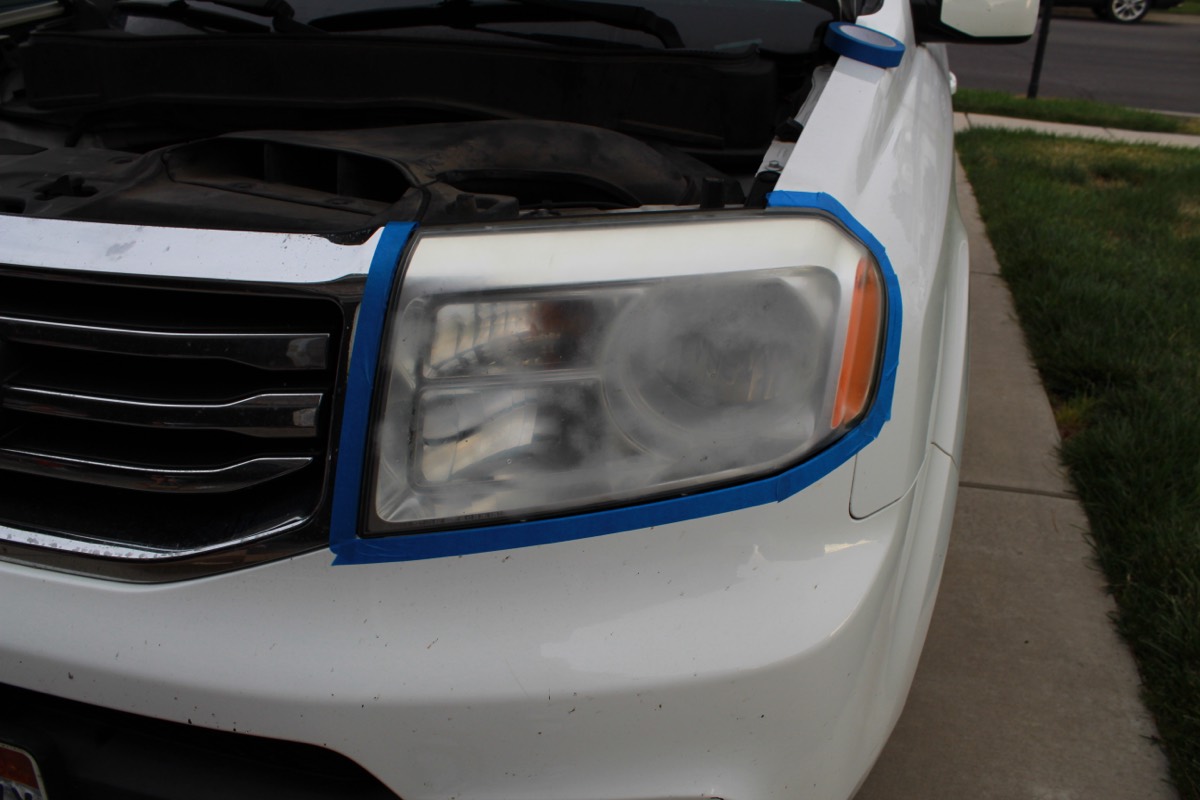Yellowed, hazy headlight lens on a white Honda Pilot, taped off before restoration